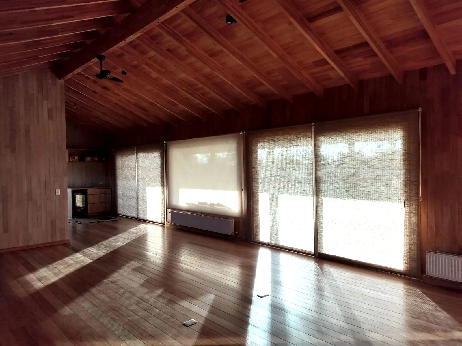Cortina roller screen en el ventanal de una casa con cielorraso de madera