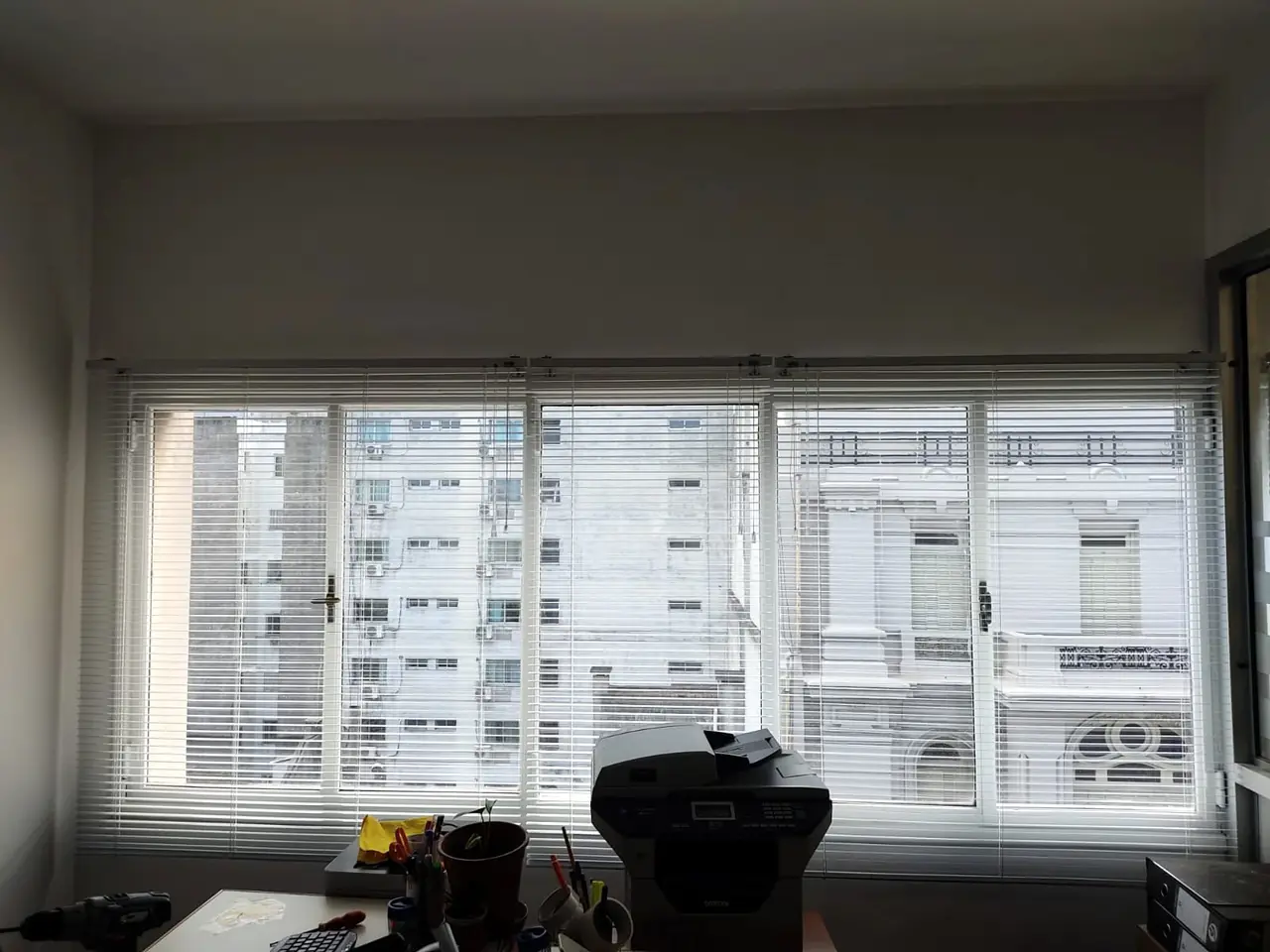 Veneciana blanca en una ventana con vista a edificios